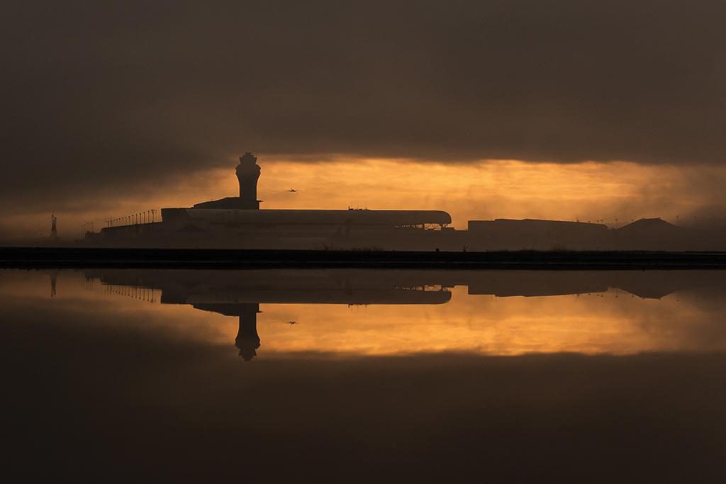 Water reflects in a puddle with the Portland International Airport flight tower in the background